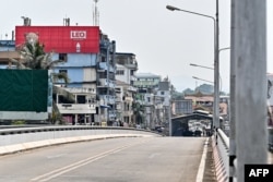 A Myanmar flag (R) flutters atop a Border control building on the Myanmar side as Myanmar nationals walk on the Thailand-Myanmar Friendship bridge, as seen from Thailand's Mae Sot district on April 12, 2024.