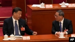 FILE - Chinese President Xi Jinping, left, chats with Chinese Premier Li Qiang during a session of China's National People's Congress at the Great Hall of the People in Beijing, March 12, 2023.