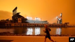 FILE - A jogger runs along McCovey Cove outside Oracle Park in San Francisco, under darkened skies from wildfire smoke on Sept. 9, 2020. 