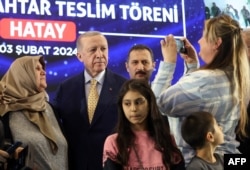Turkish President Recep Tayyip Erdogan poses for a photograph after presenting a key to a woman for a post-quake house during the Drawing and Key Handover Ceremony of Post-Quake Houses in Hatay, southern Turkey. (Photo by handout / Turkish Press Service / AFP)