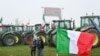 Bendera nasional Italia berkibar di depan traktor yang diparkir di sepanjang jalan saat para petani melakukan aksi protes di dekat pintu masuk jalan raya di Melegnano, dekat Milan, 30 Januari 2023. (GABRIEL BOUYS / AFP)
