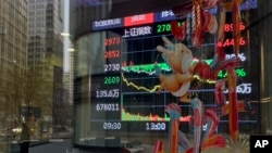 A pedestrian and office buildings are reflected on a brokerage house's window as an electronic board displaying Shanghai shares trading index in Beijing, Feb. 5, 2024. 