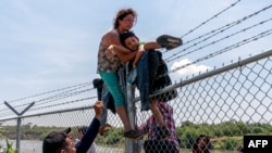 FILE - Migrants climb over a barbed wire fence after crossing the Rio Grande into US from Mexico, in Eagle Pass, Texas, Aug. 25, 2023. 