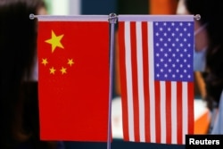 Anggota staf mengobrol di balik bendera China dan AS yang ditampilkan di China International Fair for Trade in Services (CIFTIS) 2021 di Beijing, China, 4 September 2021. (Foto: REUTERS/Florence Lo)