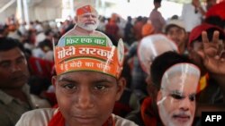 Supporters of the ruling Bharatiya Janata Party (BJP) wear party headwear and cut out masks India's Prime Minister Narendra Modi during an election campaign rally attended by Modi in Prayagraj on May 21, 2024.