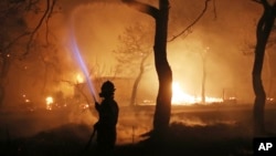 FILE - A firefighter sprays water on the fire in the town of Mati, east of Athens, July 23, 2018. An Athens court on April 29, 2024, convicted six people for their role in the response to the blaze, which left 104 people dead.