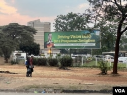 Citizens walk past a banner of President Emmerson Mnangagwa saying Zimbabwe is shaping to be prosperous by 2030 in Harare. (Columbus Mavhunga/VOA)