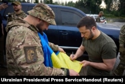 Ukraine's President Volodymyr Zelenskiy signs a national flag for a service member at a petrol station after visiting positions near the front line in Donetsk region, June 26, 2023.