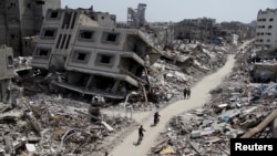 FILE - Palestinians ride bicycles past the ruins of houses and buildings destroyed during Israel’s military offensive in the northern Gaza Strip, March 31, 2024. 