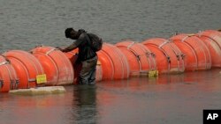 A migrant from Colombia stands at a floating buoy barrier as he looks to cross the Rio Grande from Mexico into the US, Aug. 21, 2023, in Eagle Pass, Texas. 