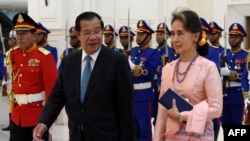 FILE - Myanmar's State Counsellor Aung San Suu Kyi (R) and Cambodia's Prime Minister Hun Sen walk past the honor guard during her visit at the Peace Palace in Phnom Penh, April 30, 2019.