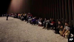 FILE - Migrants wait along a border wall Aug. 23, 2022, after crossing from Mexico near Yuma, Arizona.