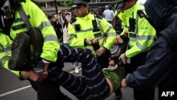 Anggota Kepolisan Metropolitan London menahan demonstran yang memblokade sebuah bus yang akan membawa para pencari suaka dari sebuha hotel di Peckham, di selatan London, pada 2 Mei 2024. (Foto: AFP/Henry Nicholls)