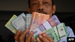 Seorang pria memperlihatkan uang kertas Rupiah baru yang akan diberikan kepada anggota keluarganya selama perayaan Idulfitri pada 28 Maret 2024. (Foto: AFP)