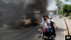 A motorcyclist drives past a burning vehicle set on fire by angry supporters of Pakistan's former Prime Minister Imran Khan, in Lahore, Pakistan, May 11, 2023.