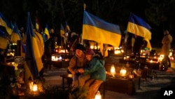 Olesia, de 41 años, y su hija Uliana, de 8, se sientan junto a la tumba de su esposo, Ihor Marchenko, en el cementerio de Lviv, Ucrania occidental, el 23 de febrero de 2023.