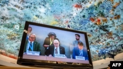U.N. High Commissioner for Human Rights Volker Turk, center, is seen on a TV monitor speaking during a session of the 52nd U.N. Human Rights Council, in Geneva, on March 6, 2023. 