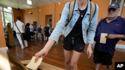 A man waits as a woman drops her ballot into a box a polling place in Redfern as Australians cast their final votes in Sydney, Oct. 14, 2023.