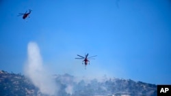 A helicopter drops water over a wildfire atop Mount Parnitha, in northwestern Athens, Greece, Aug. 24, 2023.