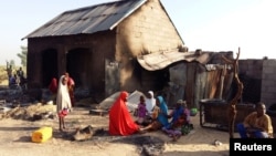 FILE - People sit near a burned house after an attack by suspected members of the Islamist Boko Haram militant group, in Bulabulin village, Nigeria, Nov. 1, 2018. 