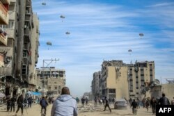 Palestinians run along a street as humanitarian aid is airdropped in Gaza City on March 1, 2024
