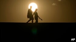 FILE - People walk along a trail as the sun sets, July 16, 2023, in Death Valley National Park, Calif.