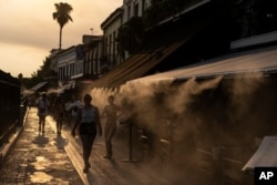 FILE - People walk next a mist machine to cool down, in Monastiraki district of Athens, July 20, 2023.
