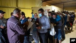 FILE - People line up for a commercial bus that will take them to the San Antonio airport at a warehouse run by the Mission: Border Hope nonprofit group run by the United Methodist Church in Eagle Pass, Texas, May 23, 2022.