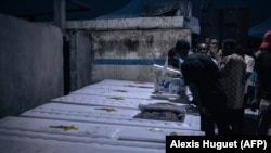 Les proches des personnes tuées fin août par l'armée à Goma, dans l'est de la RDC, regardent l'intérieur des cercueils alors qu'ils sont déchargés dans un cimetière à la périphérie de la ville, le 18 septembre 2023.