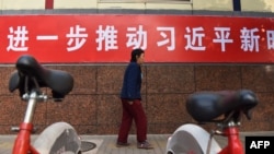 资料照：一名妇女走过北京街头宣传习近平新时代的标语。（2017年10月27日）