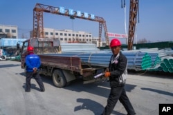Seorang pekerja berjalan melewati pipa baja yang dimuat ke truk di Xiongan di Provinsi Hebei, China utara pada 14 Maret 2024. (Foto: AP)