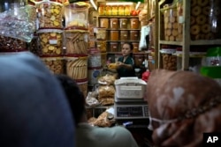 Seorang penjual tengah melayani pelanggan di toko kue dan makanan ringan di sebuah pasar di Jakarta, Kamis, 4 April 2024. (AP/Dita Alangkara)