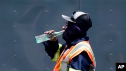FILE - Standing in the heat, a worker takes a drink during a parking lot asphalt resurfacing job in Richardson, Texas, June 20, 2023. A sweeping new law in Texas targets local regulations.