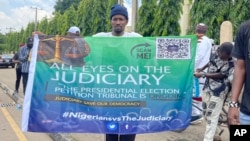 A man holds a banner in Abuja, Nigeria, Sept. 6, 2023, as Nigeria's presidential tribunal met to deliver its judgment on the disputed election of Bola Tinubu as president. The tribunal upheld the election.