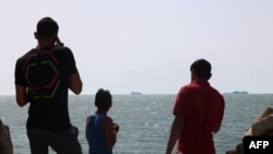 Palestinian youths stand on a jetty in Gaza City with a view of navy vessels as part of a humanitarian 'maritime corridor' announced by US Central Command (CENTCOM) on May 17, 2024.