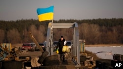 A woman crosses a makeshift pedestrian bridge connecting the two sides of a destroyed road bridge in Staryi Saltiv, Ukraine, Feb. 17, 2023.