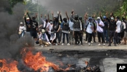 FILE - Anti-coup protesters gesture with a three-fingers salute, a symbol of resistance to the military junta, during a police crackdown in Thaketa township, Yangon, Myanmar, March 27, 2021.