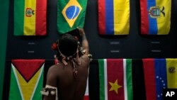 An indigenous man passes his hand over the Brazilian flag in a flag pavilion of the States parties to the Amazon Cooperation Treaty, during the Amazon Dialogue meetings at the Hangar convention center in Belem, Brazil, Aug. 6, 2023. 