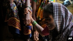 FILE - A woman holds the hand of her relative as family members of people trapped under rubble wail after a landslide washed away houses in Raigad district, western Maharashtra state, India, July 20, 2023.