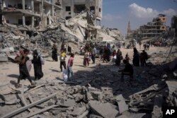 Warga Palestina berjalan melewati puing-puing bangunan yang hancur setelah serangan udara dan darat Israel di Khan Younis, Jalur Gaza selatan, Senin 8 April 2024.