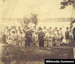This 1865 photograph shows French missionary Eugene Casimir Chirouse (left) and an unidentified priest standing with students at the Tulalip Mission School, Tulalip, Washington.