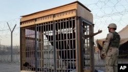 FILE - In this June 22, 2004, photo, a detainee in an outdoor solitary confinement cell talks with a military police officer at the Abu Ghraib prison on the outskirts of Baghdad, Iraq.