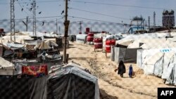 FILE - A woman and a child walk between tents at the Kurdish-run al-Hol camp which holds suspected relatives of Islamic State group fighters, in Hasakeh governorate of northeastern Syria, on March 3, 2021.