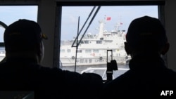 Philippine coast guard members observe a Chinese coast guard ship blocking their path during a re-supply mission by a civilian boat chartered by the Philippine navy to deliver supplies to a Philippine navy ship in the disputed South China Sea, Aug. 22, 2023.