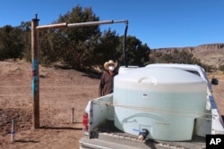FILE - Phillip Yazzie waits for a water drum in the back of his pickup truck to be filled in Teesto, Arizona, on the Navajo Nation, Feb. 11, 2021.