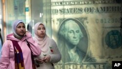 FILE - Egyptians walk past a poster depicting a US dollar outside an exchange office in Cairo, Feb. 9, 2023.
