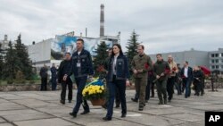 Chernobyl nuclear power plant workers carry flowers to the monument honoring victims of the 1986 explosion and fire at the plant in Chernobyl, Ukraine, April 26, 2023.