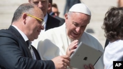 FILE - Pope Francis looks at an iPad at the end of his weekly general audience, in St. Peter's Square at the Vatican, June 7, 2017. (L'Osservatore Romano/Pool Photo via AP)
