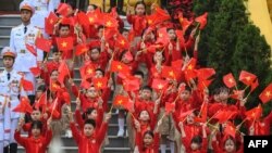 FILE - Children wave Vietnamese national flags during a welcome ceremony for China's President Xi Jinping at the Presidential Palace in Hanoi, Dec. 12, 2023.