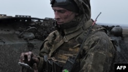 FILE - A Ukrainian soldier uses his mobile phone on front line near Bakhmut, in Ukraine's Donetsk region, partially occupied by Russian forces, March 11, 2023.